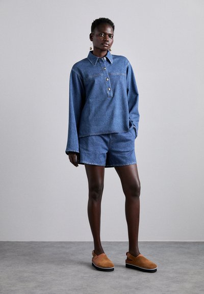 Denim krekls ar apkakli un pogu rindas, saskaņots ar atbilstošiem denim šortiem. Smilškrāsas zamšādas iešļūcenes noslēdz komplektu.