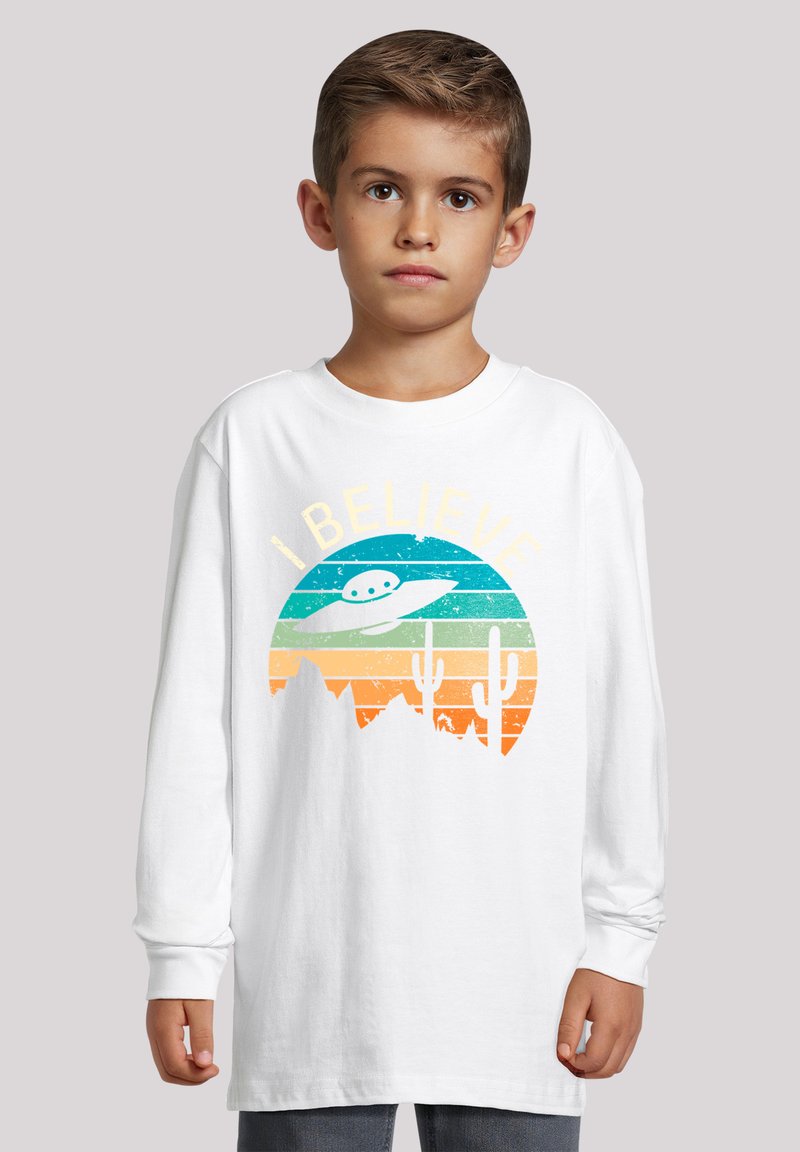 Weißes Langarm-T-Shirt mit einem bunten, retro UFO-Design und dem Text "ICH GLAUBE", auf einem Farbverlauf-Hintergrund eines Sonnenuntergangs.