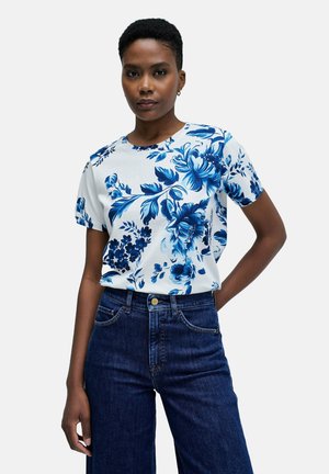 Camiseta de manga corta floral en blanco con patrones de flores azules, combinada con jeans de talle alto de mezclilla oscura. Textura de tela suave.