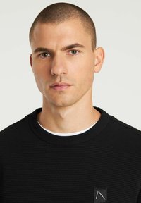 Schwarzer, gerippter Sweatshirt mit Rundhalsausschnitt und weißem Innenkragen. Verfügt über ein kleines Logo-Patch auf der Brust. Glatte Textur, taillierte Passform.