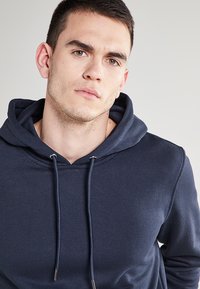 Sudadera azul marino con una textura suave, capucha y cordones de tono plateado. Presenta un diseño simple y sin patrones o logotipos visibles.