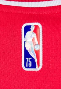 Maillot rouge avec une surface texturée, arborant un patch holographique du logo NBA en bleu, blanc et rouge, représentant un joueur dribblant un ballon de basket et le numéro "75".