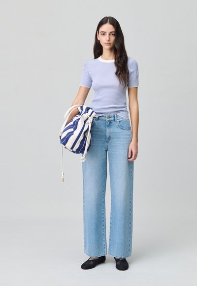 Top corto a maniche corte di un azzurro chiaro a coste, jeans in denim chiaro a vita alta, e una borsa a strisce con cordoncino blu e bianco. Scarpe in rete nere.