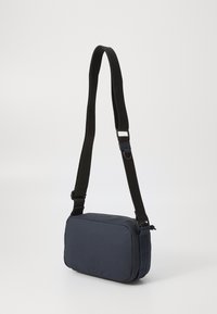 Námornícky crossbody vak vyrobený z odolnej textílie, s obdĺžnikovým tvarom, nastaviteľným čiernym popruhom a kontrastným šitím.