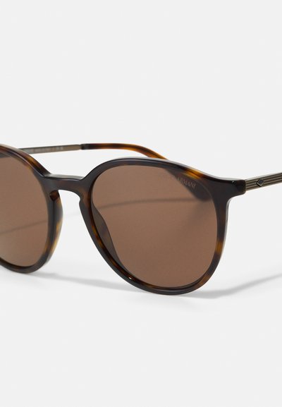 Brown-tinted oval sunglasses with tortoiseshell-patterned frames and subtle metal accents on the sides. Elegant and lightweight design.
