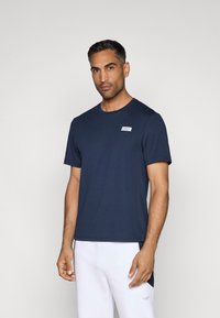 Sötétkék, rövid ujjú póló, puha anyagból, bal mellrészen egy kis fehér címkével és klasszikus kerek nyakkivágással.