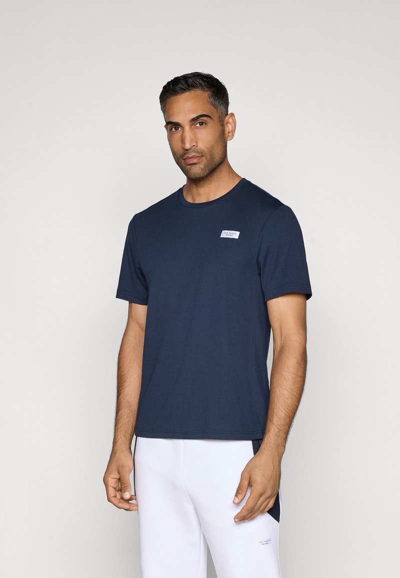 Sötétkék, rövid ujjú póló, puha anyagból, bal mellrészen egy kis fehér címkével és klasszikus kerek nyakkivágással.