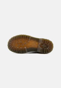 Semelle d'une botte translucide marron avec des motifs de crampons profonds, incluant des dessins en forme de fleurs et des rainures d'adhérence épaisses.