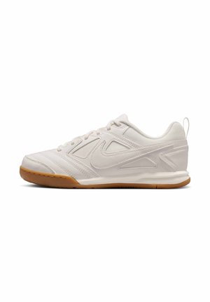 Chaussure de sport blanche avec une tige synthétique lisse, des accents texturés et une semelle extérieure en caoutchouc naturel. Dispose d'un système de laçage et d'une languette à l'arrière.