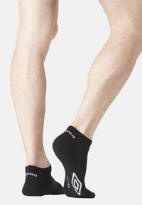 Chaussettes noires de cheville en tissu doux, avec un logo blanc et un motif en diamant sur le talon, offrant un ajustement ajusté autour de la cheville.