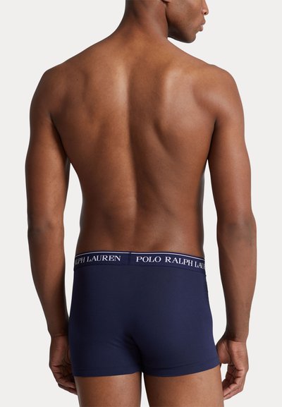 Modèle masculin vu de dos, portant un boxer Polo Ralph Lauren bleu marine avec une ceinture logo sur un fond uni.