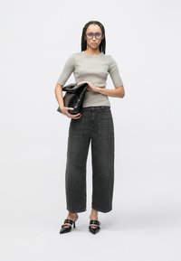 Šedý přiléhavý top, tmavé široké džíny s předními kapsami, černá lesklá kabelka do ruky a černé lodičky s špičatou špičkou a zdobením popruhy.