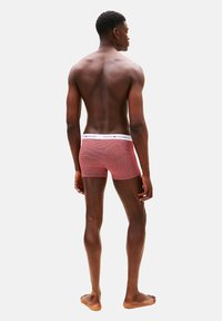 Boxer rojo con estampado y una cintura elástica blanca con el nombre de la marca. La tela parece suave y elástica.