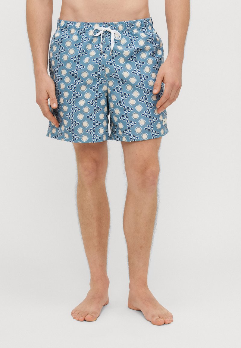 Peldbikses, kas izgatavotas no viegla auduma, ar zilu fonu, kas rotāts ar baltām ziedu un apļu rakstiem, elastīgu jostu un aukliņu.