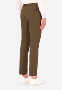 Pantaloni chino marroni slim-fit con tasche posteriori e un discreto marchio; abbinati a sneakers bianche e un maglione crema.