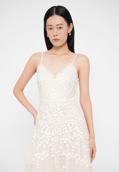 Λευκό φόρεμα από δαντέλα με λουλούδια, με εφαρμοστή μπούστα, λεπτές τιράντες, V-λαιμόκοψη και φούστα που ρέει, διακοσμημένη με κεντημένα λουλούδια.