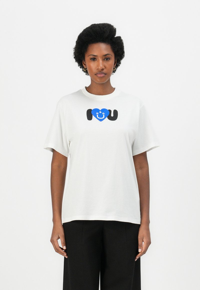 Witte katoenen T-shirt met korte mouwen, met een graphic print van een blauwe hart en de tekst "Ik ❤️ U" in zwart. Eenvoudig ontwerp met ronde hals.