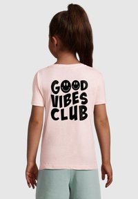 Svijetlo ružičasta majica kratkih rukava s velikim crnim natpisom "GOOD VIBES CLUB" i dva smajlića na leđima. Mekani materijal, ležeran kroj.