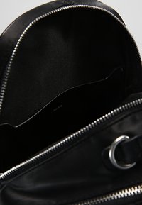 Avoin musta laukku, jossa on näkyvä sisätasku ja hopeiset vetoketju-yksityiskohdat, näyttäen sileää kangasta vuorauksena ja metallirenkaana ulkopuolella.