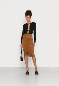 Bodysuit preto de mangas longas com recortes circulares ao centro, combinado com uma saia midi franzida na cor castanha e sandálias trançadas pretas.