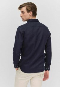 Marineblauwe overhemd met lange mouwen en een button-down kraag, gemaakt van textuurstof, met een afgeronde onderkant en knoopmanchetten.