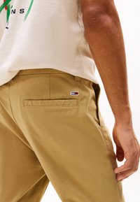 Chinos caqui con una textura suave; presentan un bolsillo trasero con un pequeño logotipo bordado en rojo, blanco y azul.