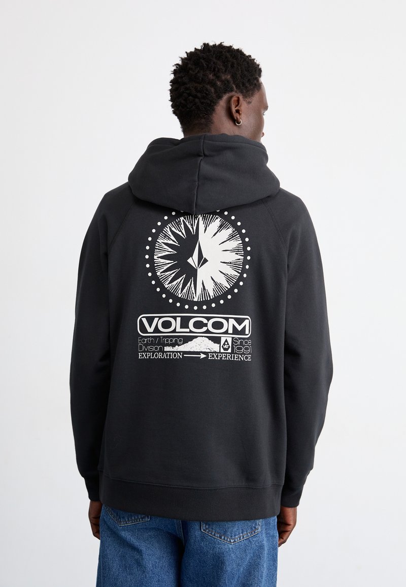 Fekete kapucnis pulóver, állítható zsinórral, a hátsó részén nagy fehér grafikával, amely egy iránytűt és szöveges részleteket ábrázol.