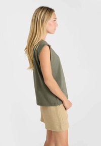 Top sans manches vert olive en tissu doux, associé à un short beige clair, avec une coupe décontractée et un design minimaliste.
