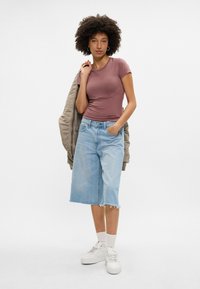 Lühikeste varrukatega mauvē värvi topp, mis on kombineeritud helesinise denimpikkade seeliku ja valgete sportlike tossudega. Riietusele lisab sooja helebeež müts.