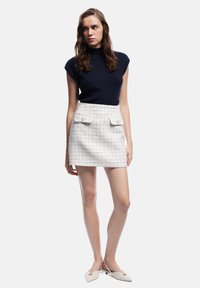 Top de punto azul marino con mangas cortas, combinado con una mini falda blanca texturizada que cuenta con dos bolsillos de solapa y detalles de botones. Zapatos de color claro.