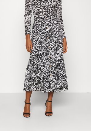 Czarna i biała abstrakcyjna sukienka midi na długi rękaw, zapinana na guziki, zestawiona z czarnymi sandałami na obcasie z paskiem wokół kostki.