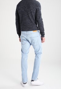 Jeans de mezclilla azul claro con un corte recto, cinco bolsillos y una etiqueta de cuero en la parte trasera de la cintura, combinados con un suéter oscuro y zapatillas blancas.