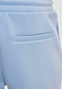 Hemelsblauwe joggingsbroek met een vlakke zak op de achterkant, gemaakt van zachte stof met een gladde textuur en een elastische tailleband voor comfort.