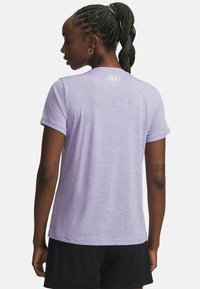 Lila korte mouwen sportshirt van textuurstof, met een logo op de achterkant. Gecombineerd met zwarte mesh shorts.