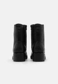 Botas de tobillo de cuero negro con una textura suave, caña alta y suela gruesa con un sutil patrón de relieve; cierre de cremallera lateral.