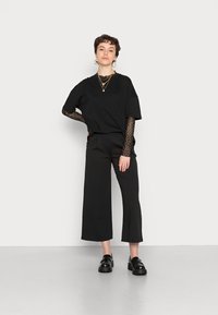 Zwarte oversized t-shirt over een zwart met stippen lange mouwen top, in combinatie met wijde zwarte broek en stevige zwarte loafers.