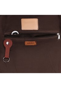Interno di una borsa marrone che mostra una tasca con cerniera con un piccolo dispositivo bianco all’interno e un portachiavi in pelle attaccato a un bottone automatico.