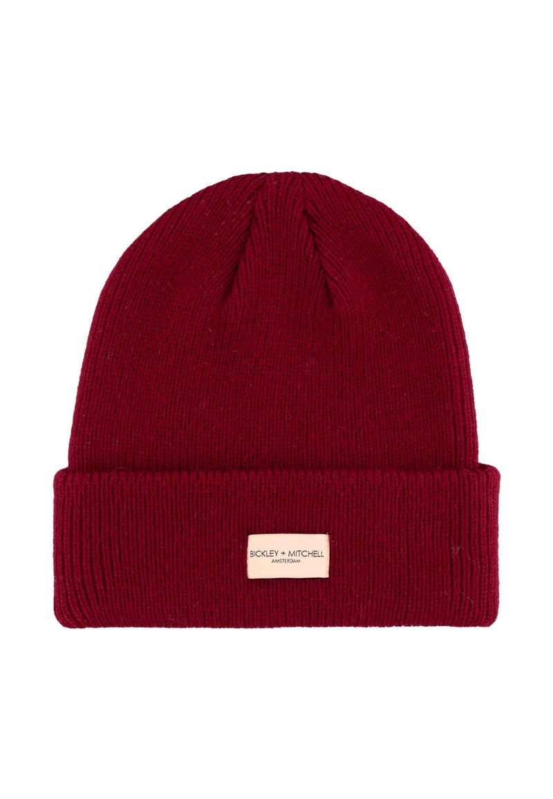 Dieprode gebreide muts met een omgeslagen rand, voorzien van een klein rechthoekig merklabel in beige aan de voorkant genaaid.