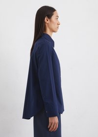Navy blue button-up shirt with a collar, long sleeves, and a curved hem. Smooth fabric with a minimalist design and no visible patterns.