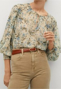 Floral blouse in cream with blue flowers, puff sleeves, and a keyhole neck. Paired with beige high-waisted pants and a brown belt.