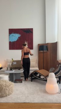 Kartonová krabice označená "Zalando" na mramorovém konferenčním stolku, béžové sedačce, dřevěné lampě a bílém, osvětleném lucerně na světlejším koberci.