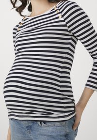 Randig graviditetstopp i svart och vitt med tre knappar på axeln, med en figurnära passform och mjukt, elastiskt tyg.