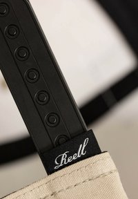 Mango negro de plástico con acentos circulares texturizados, unido a una correa de tejido color crema que presenta una etiqueta negra con letras blancas.