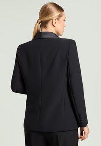 Schwarzer maßgeschneiderter Blazer aus glattem Stoff. Verfügt über ein strukturiertes Design, Revers mit Kerbe und geknöpfte Manschetten. Klare Linien ohne Verzierungen.