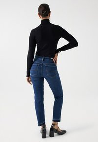 Top negro de manga larga combinado con vaqueros de mezclilla azules de tiro alto. Los vaqueros cuentan con bolsillos traseros, costuras en contraste y un diseño de pierna ajustada.