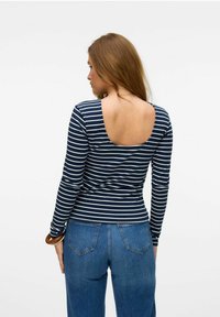 Marinblå och vit randig långärmad topp med bred halsringning och ribbad textur, i kombination med högmidjade blå denimjeans.