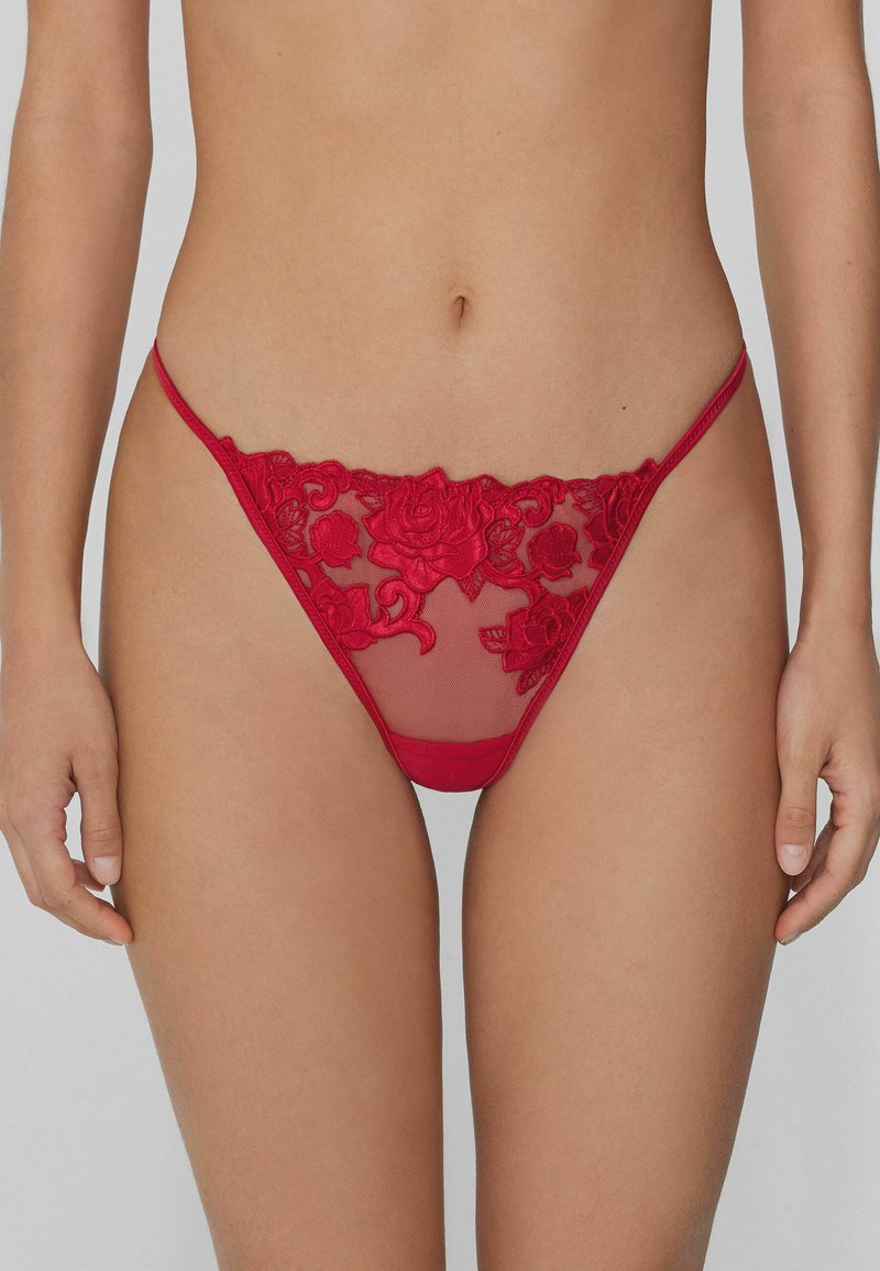 Tanga rojo bordado con un diseño de encaje floral y paneles de malla transparente. La cinturilla es delgada, lo que realza su apariencia delicada.