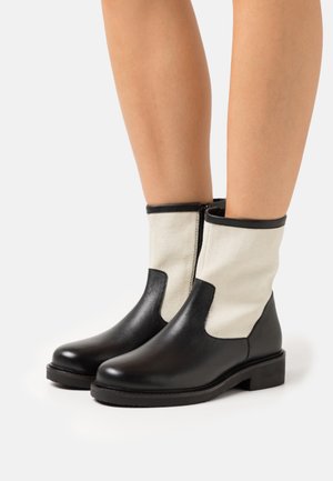 Botas de tornozelo de couro preto com laterais de lona bege, com um acabamento liso, ponta arredondada e um salto bloco baixo. Fecho com zipper de um lado.
