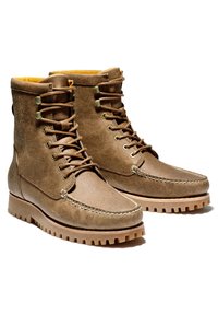 Hnědé kožené boty s hladkým povrchem, šněrovacím designem, žlutou podšívkou a robustní gumovou podrážkou s výrazným vzorkem.