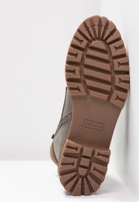 Semelle en caoutchouc marron avec un motif de grip texturé ; détail de fermeture éclair sur le côté ; partie supérieure en tissu gris avec une finition lisse. Taille 38 marquée sur la semelle.